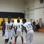 Boys basketball team dribbling and shooting hoops in a gymnasium.