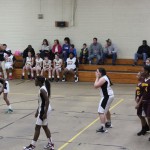 Girls playing basketball in a gymnasium, dribbling and shooting hoops.