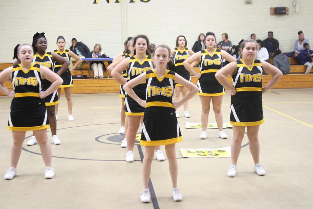 Cheerleaders in black and yellow uniforms posing in a gym.