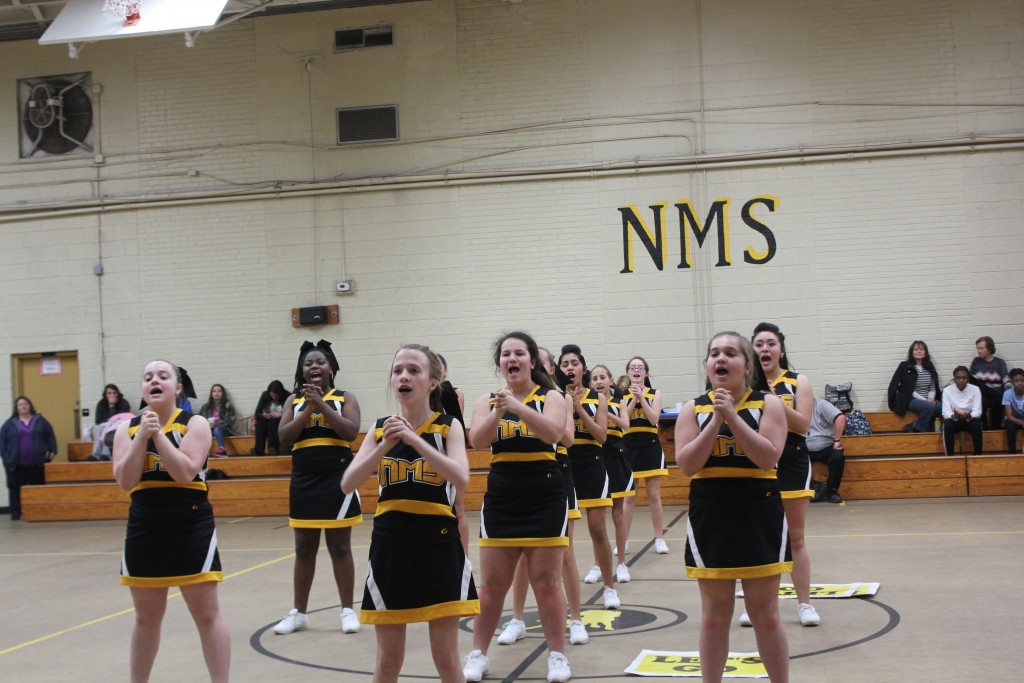 Cheerleaders in black and yellow uniforms posing in a gym.