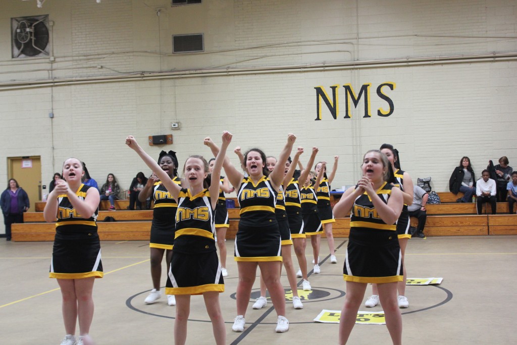 Cheerleaders in black and yellow uniforms posing in a gym.