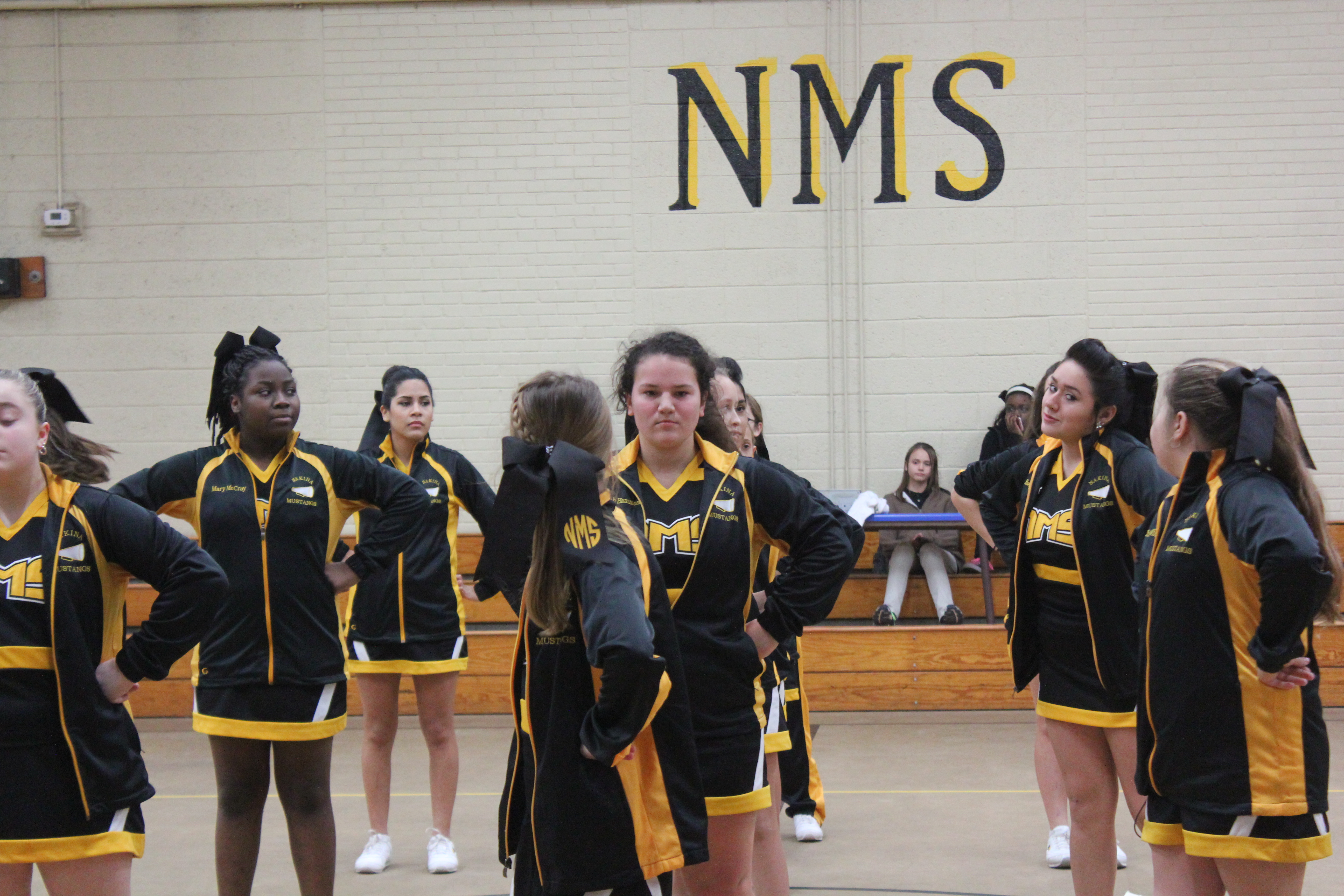 Cheerleaders in black and yellow uniforms posing in a gym.