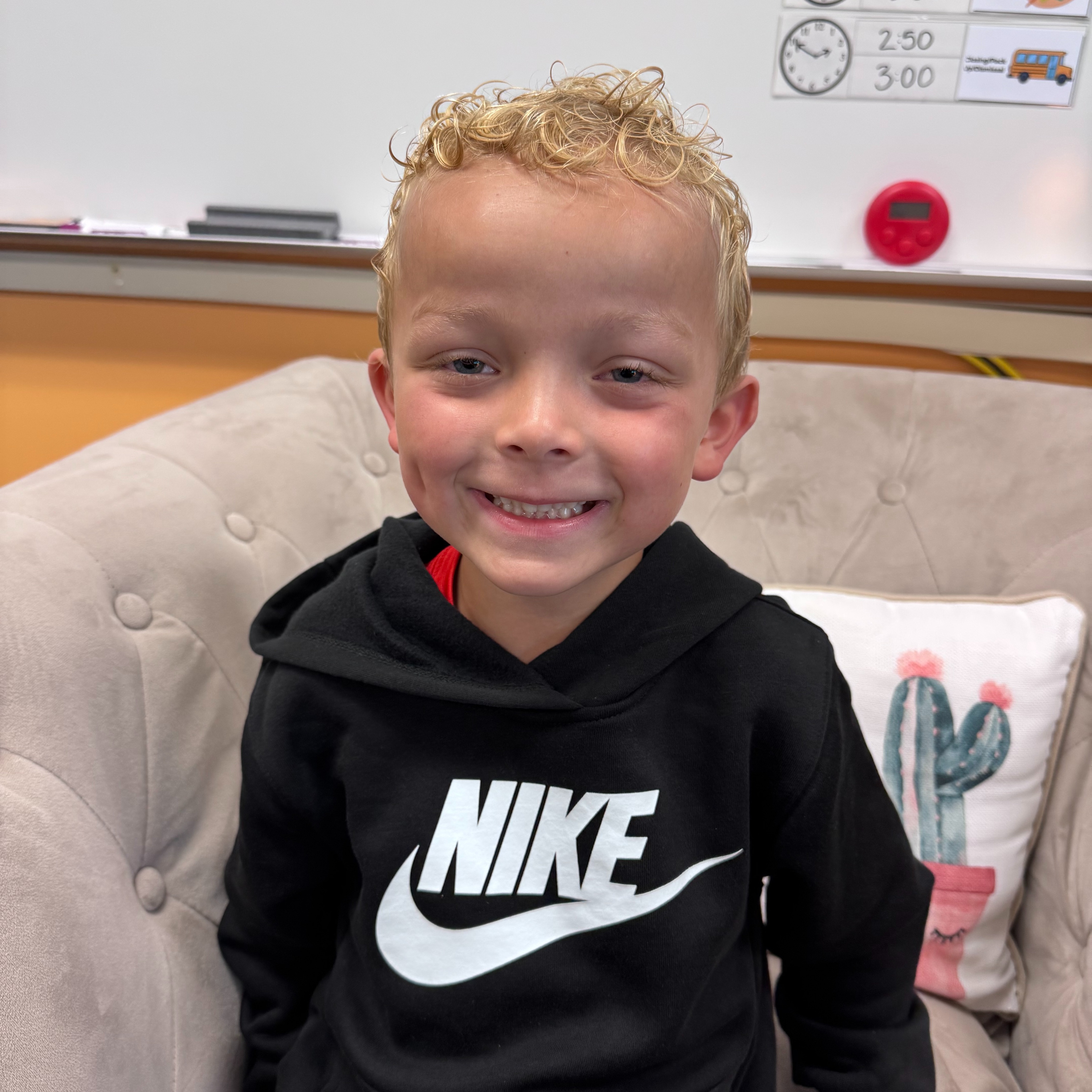 A boy in a black hoodie with the Nike logo smiles and sits on a couch.