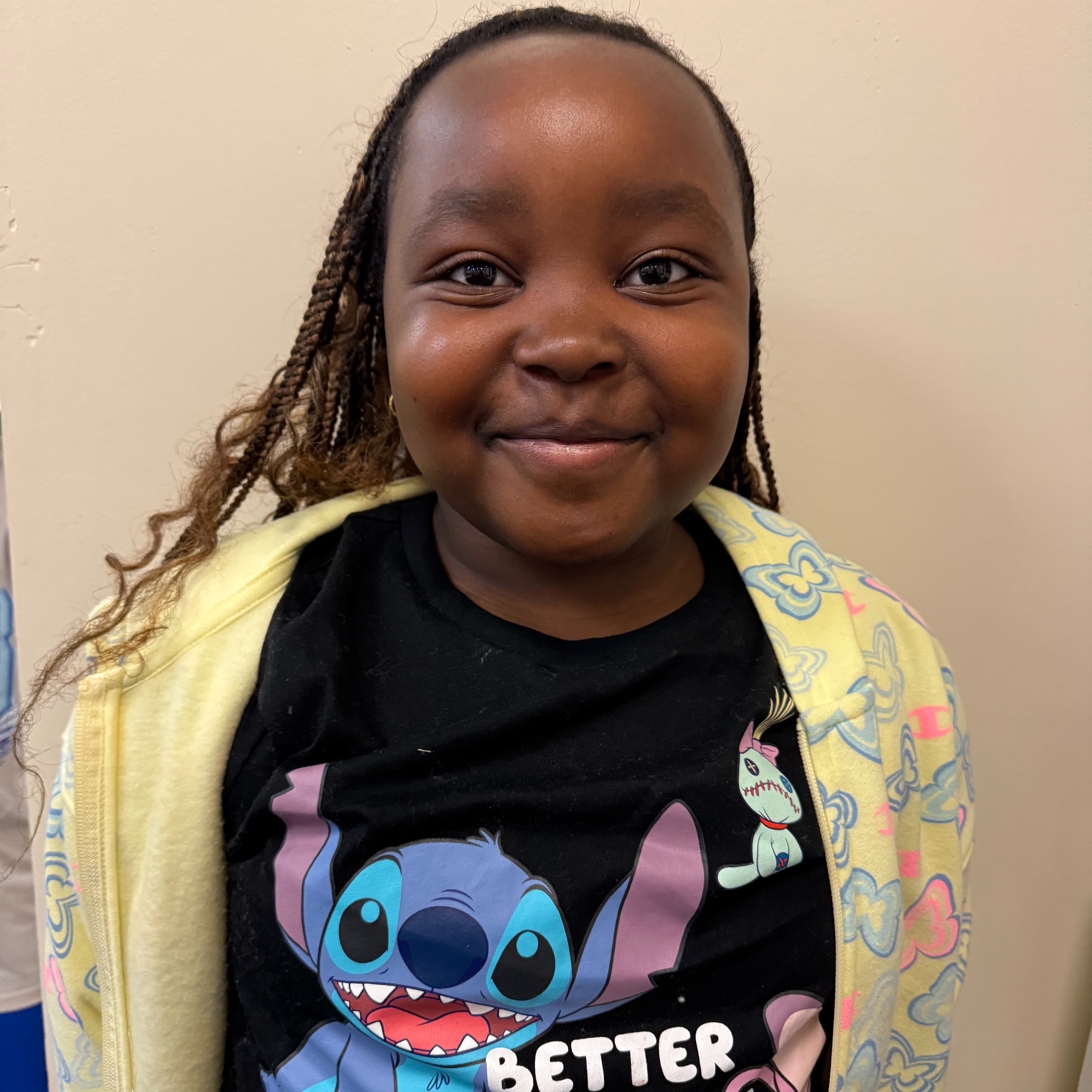 A young girl smiles, wearing a black t-shirt with a Stitch design and a yellow cardigan.