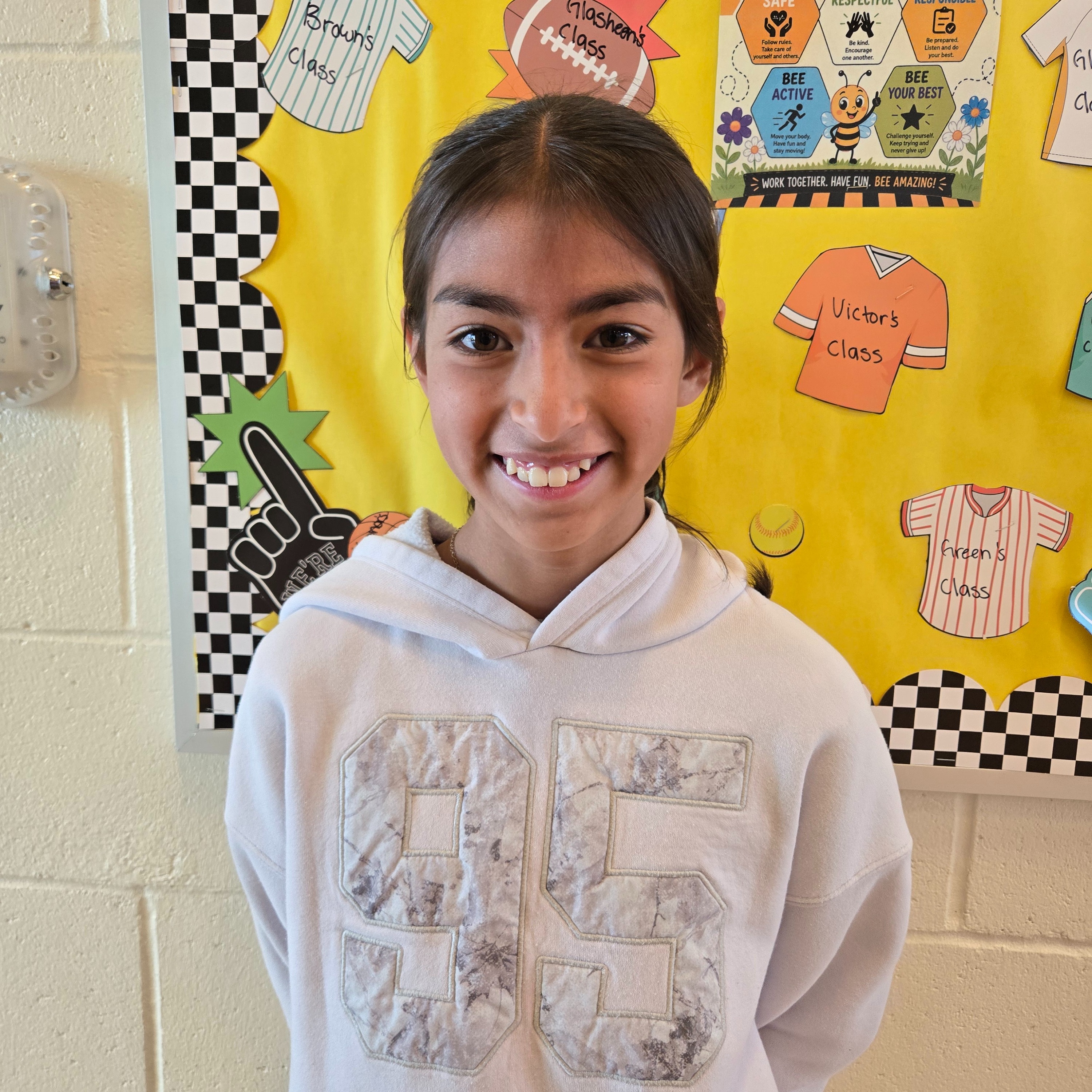 A girl in a white hoodie with "55" on it stands in front of a bulletin board.