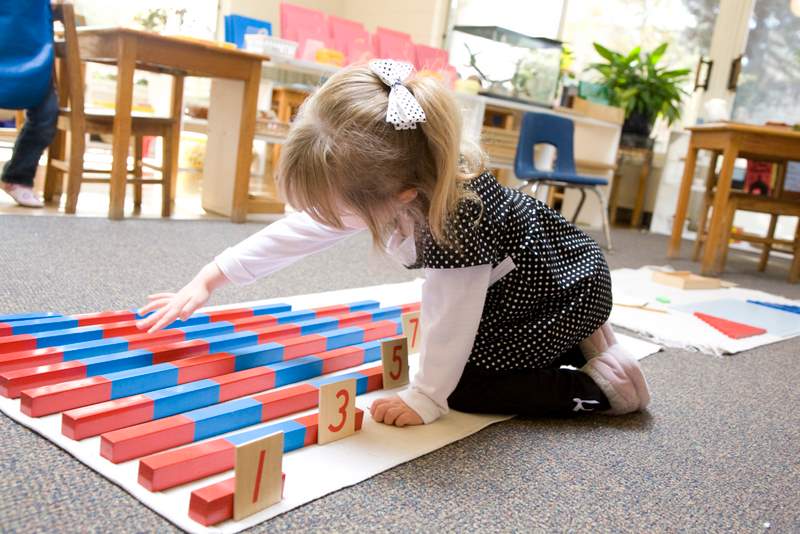 A young girl happily building with wooden blocks in a classroom.