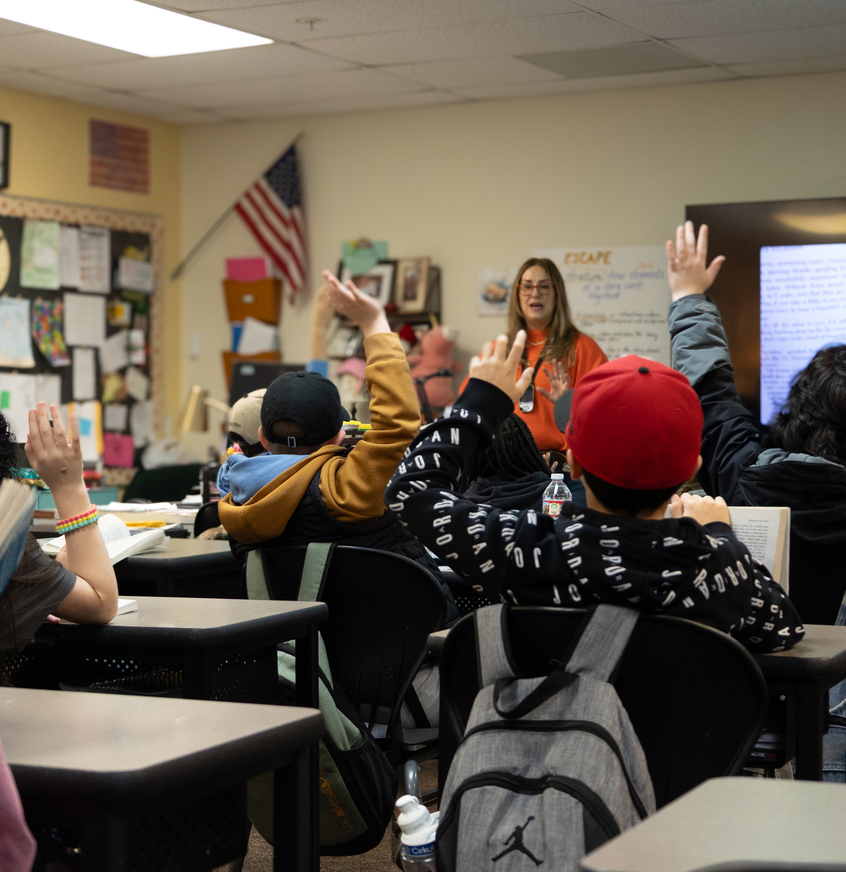 Students raise their hands in a classroom with a teacher