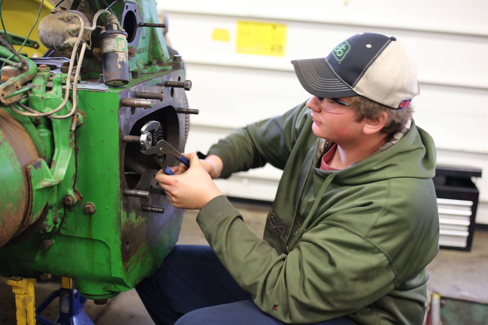 student with a hat and glasses fixing a cars wheel