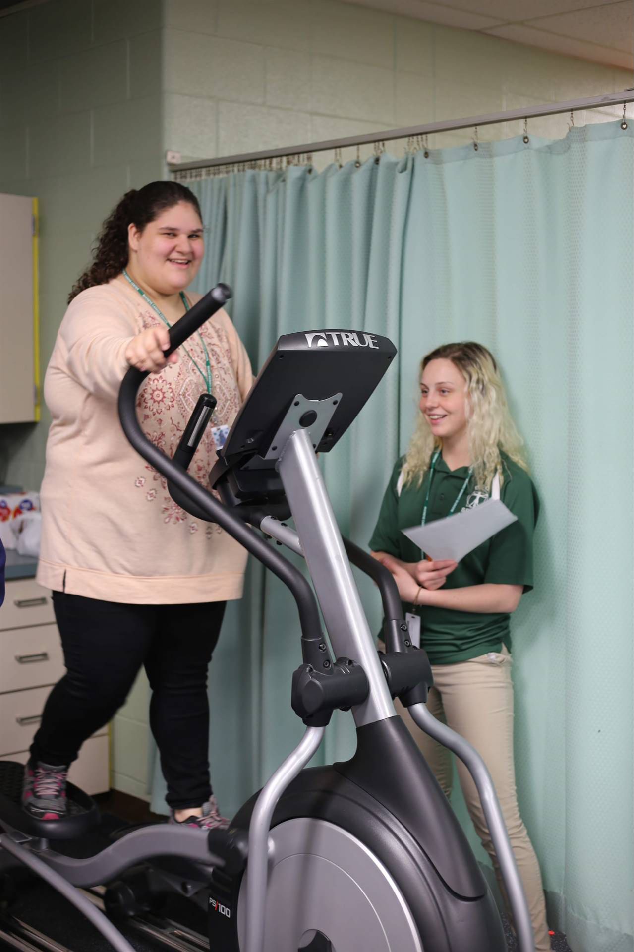 student doing exercise on the walking machine with a girl standing next to her