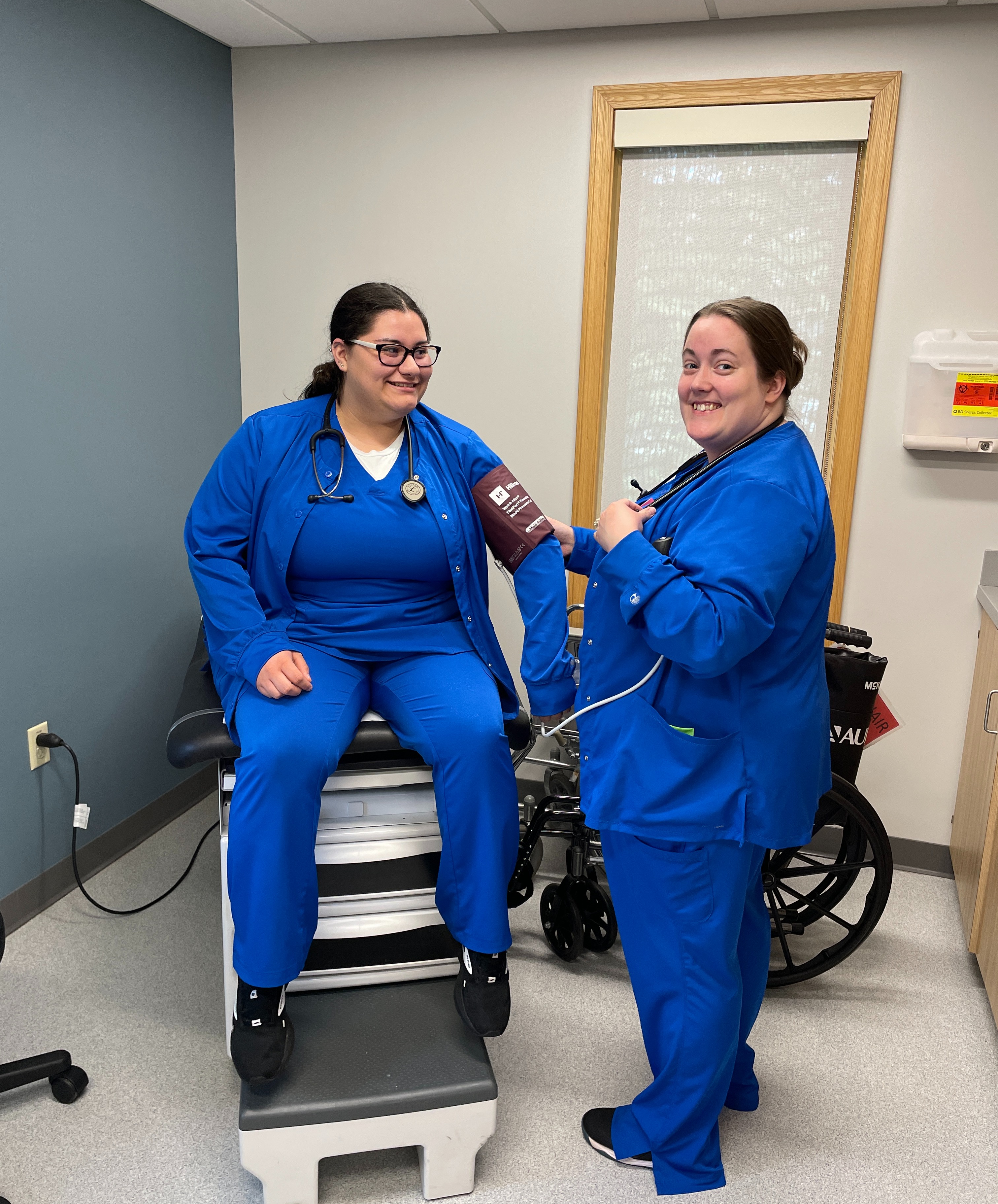 female student checking blood pressure of another student in a dr's office