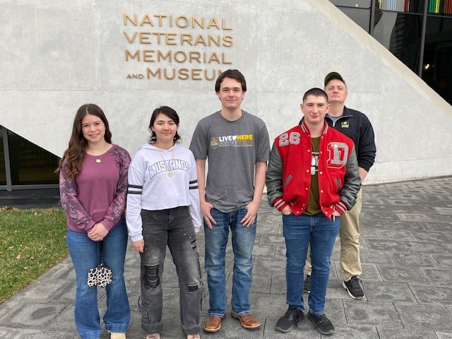 2025 enlistees posing for photo, National Veterans Memorial Museum on the background