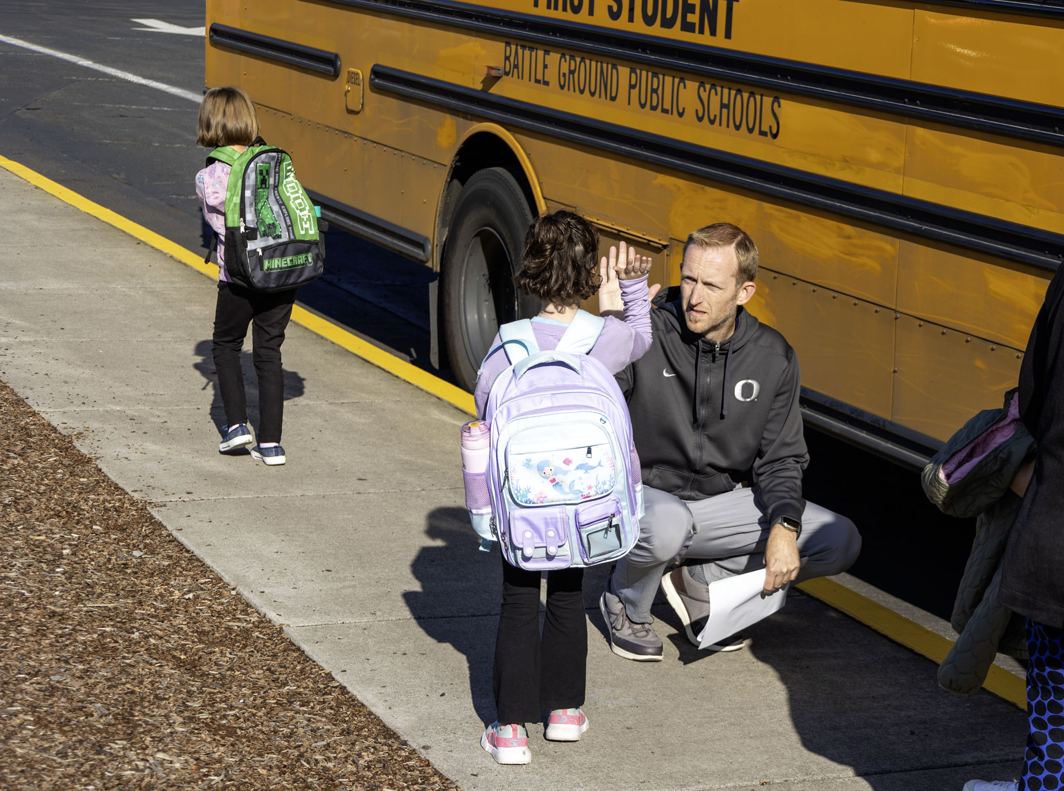 Adults greeting students getting off of a school bus