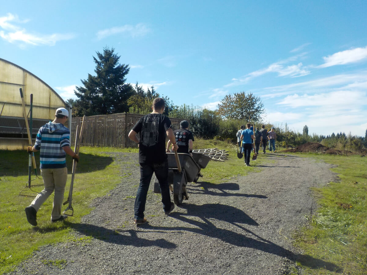 People walking on a gravel path with shovels in their hands, under a sunny sky.