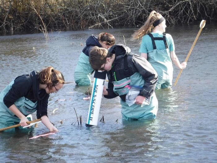 A group of people wearing waders are measuring the depth of a flooded area with sticks.