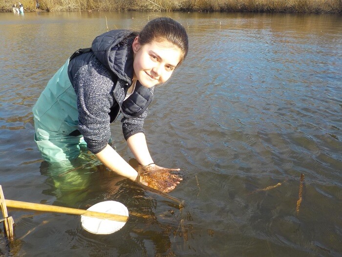 A young girl is standing in a shallow body of water, holding a small fish.