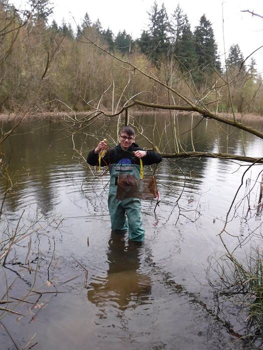 A person standing in a shallow river, fishing.