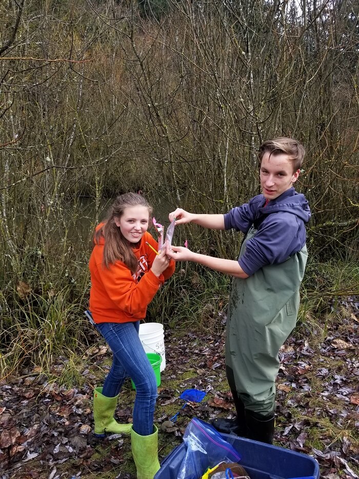 A young couple standing near a river, with one person holding a fishing rod.