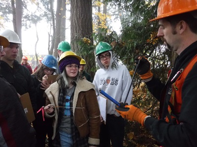 Several people gathered around a man in an orange vest, who is showing them something.