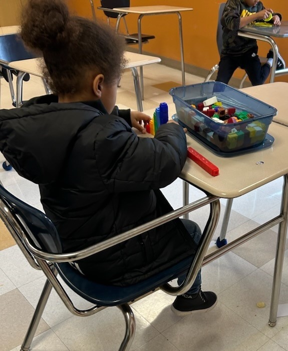 A young girl sitting at a table with a toy in front of her.