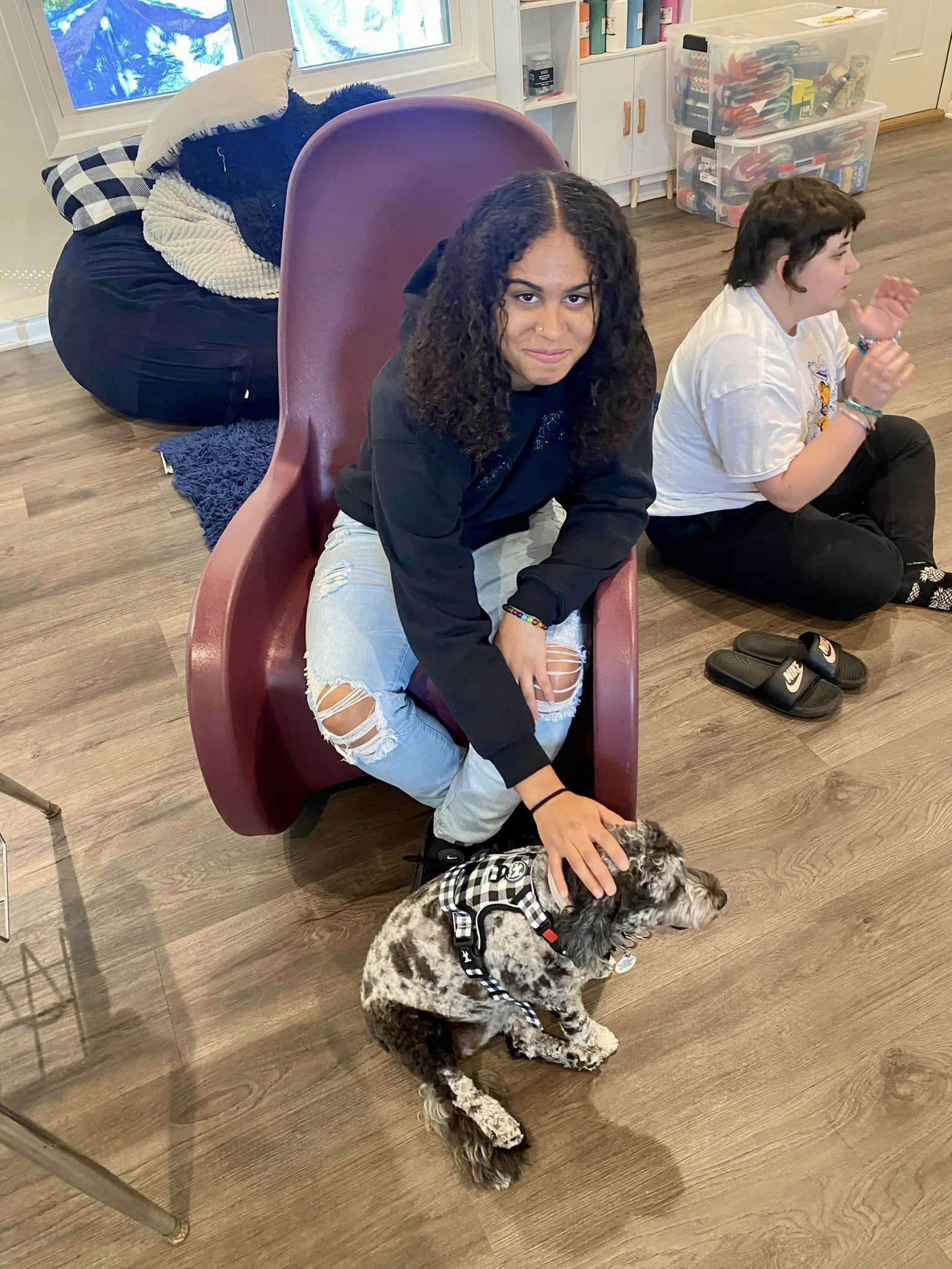 A woman sitting on a chair with a dog by her side.