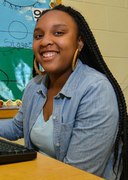 A young woman smiling at a desk with a computer.