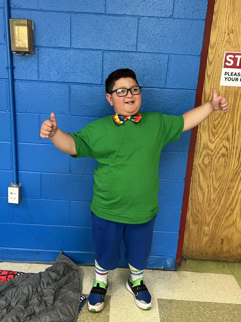 Smiling boy with glasses and green shirt showing thumbs up sign.