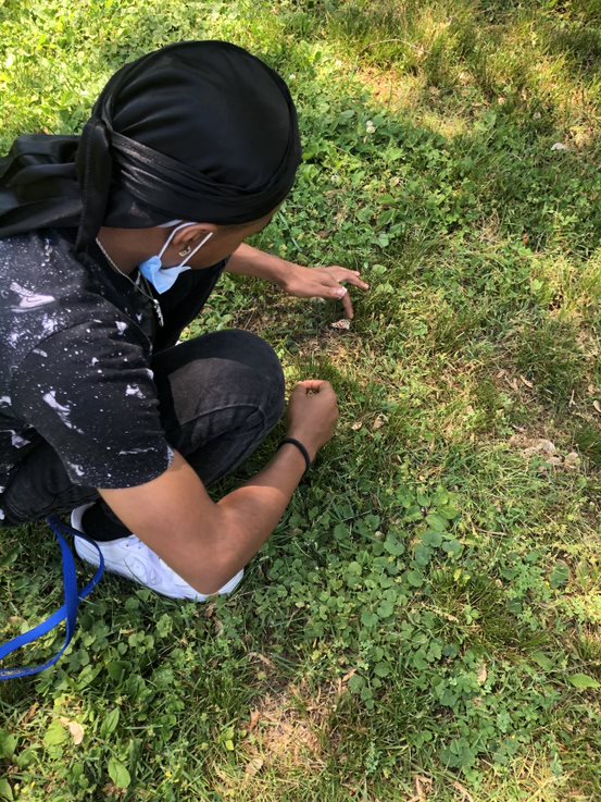 A person kneeling down in the grass with a hat on
