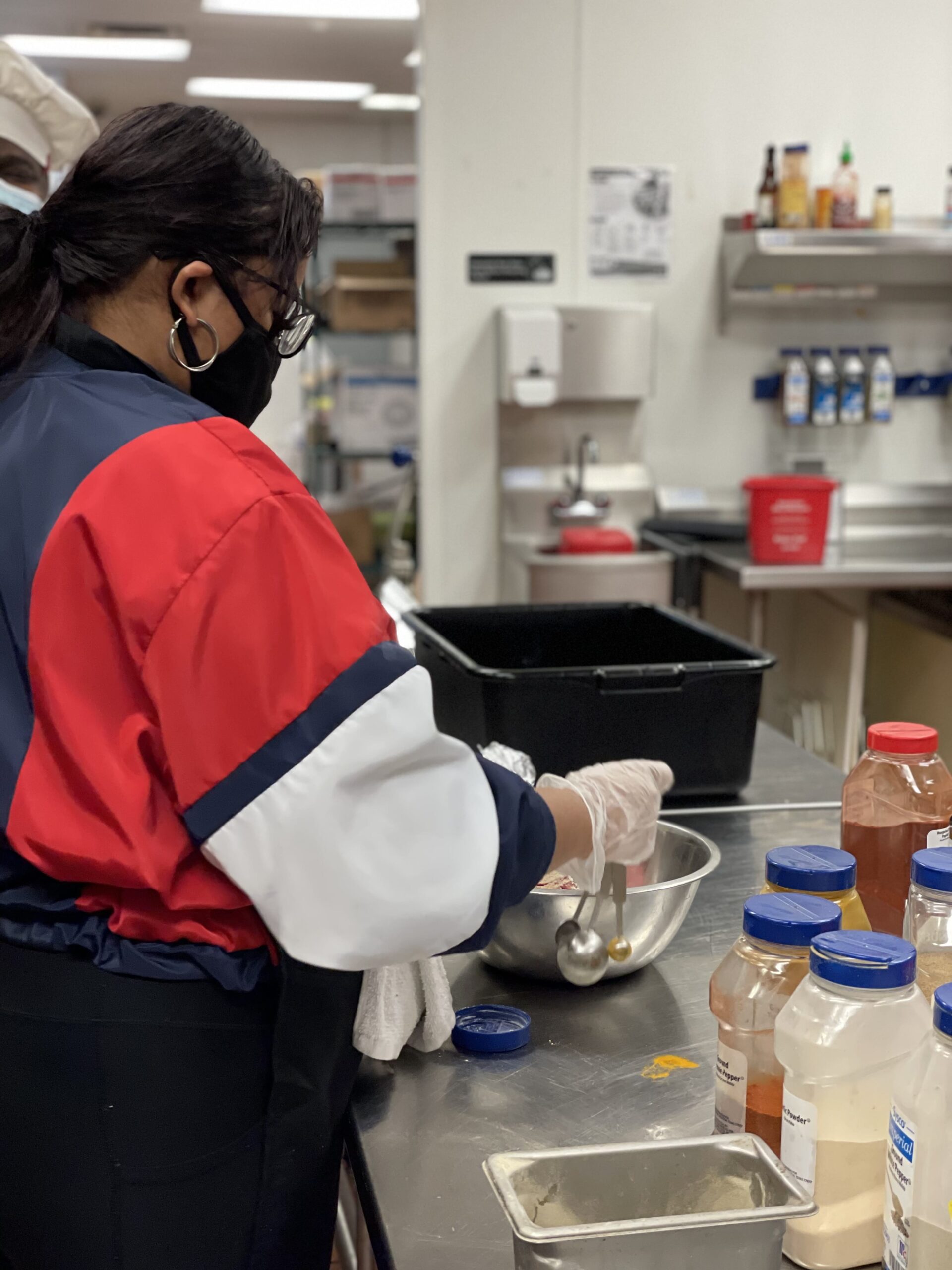 A woman in a red and white jacket cooking in the kitchen.