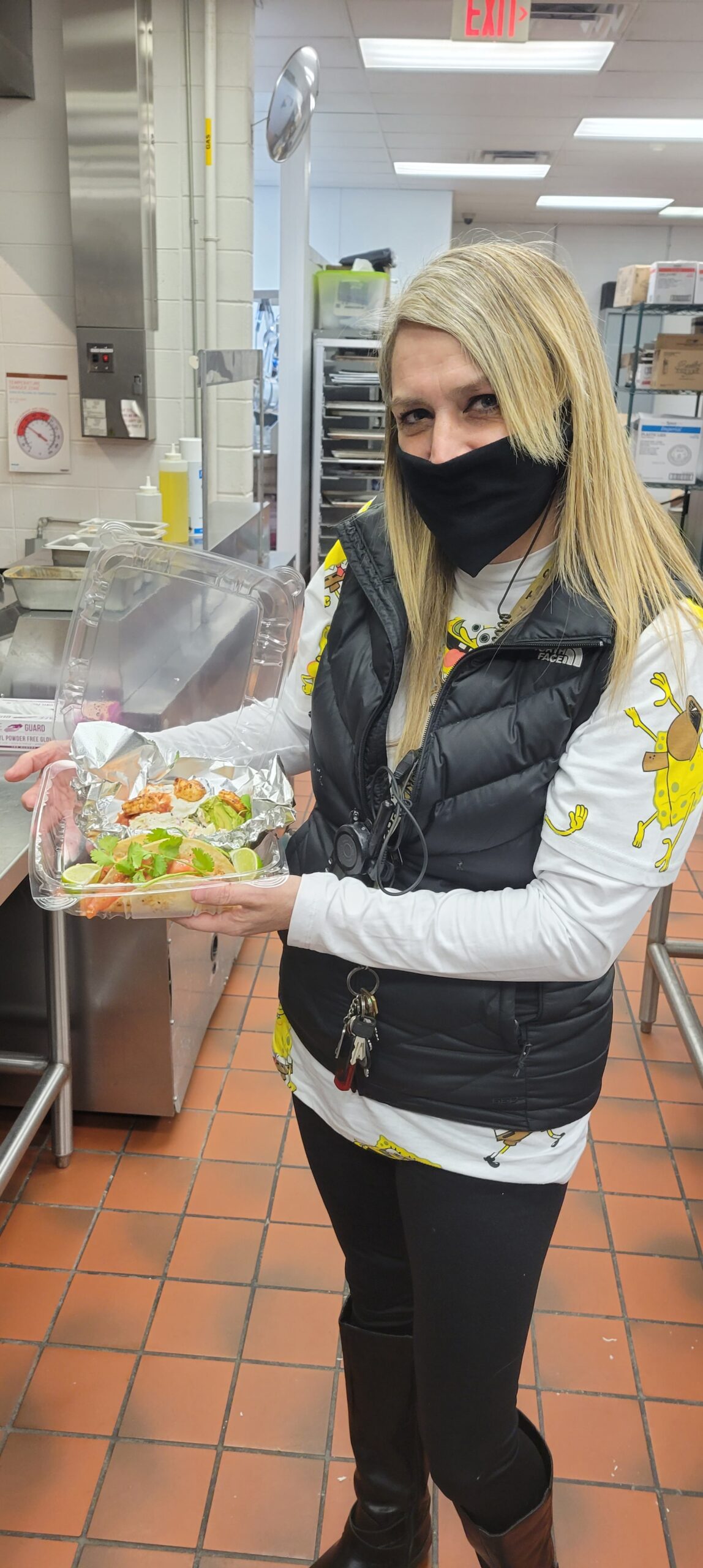 Woman wearing mask, holding tray of food.