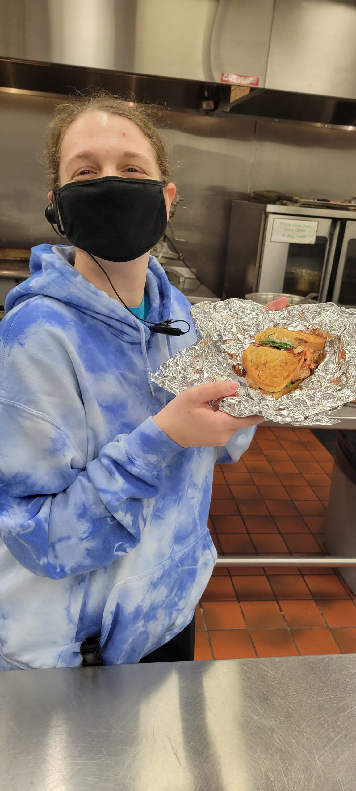 Woman wearing mask, holding tray of food.