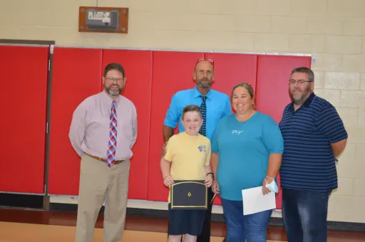 Administrators and teachers stand around a student who just won an award.