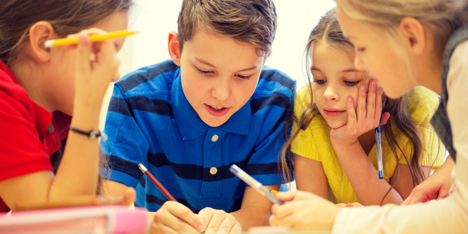 Students sitting around a desk writing with markers