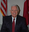 A man in a suit and tie is seated at a desk, focused on his work in a professional office environment.