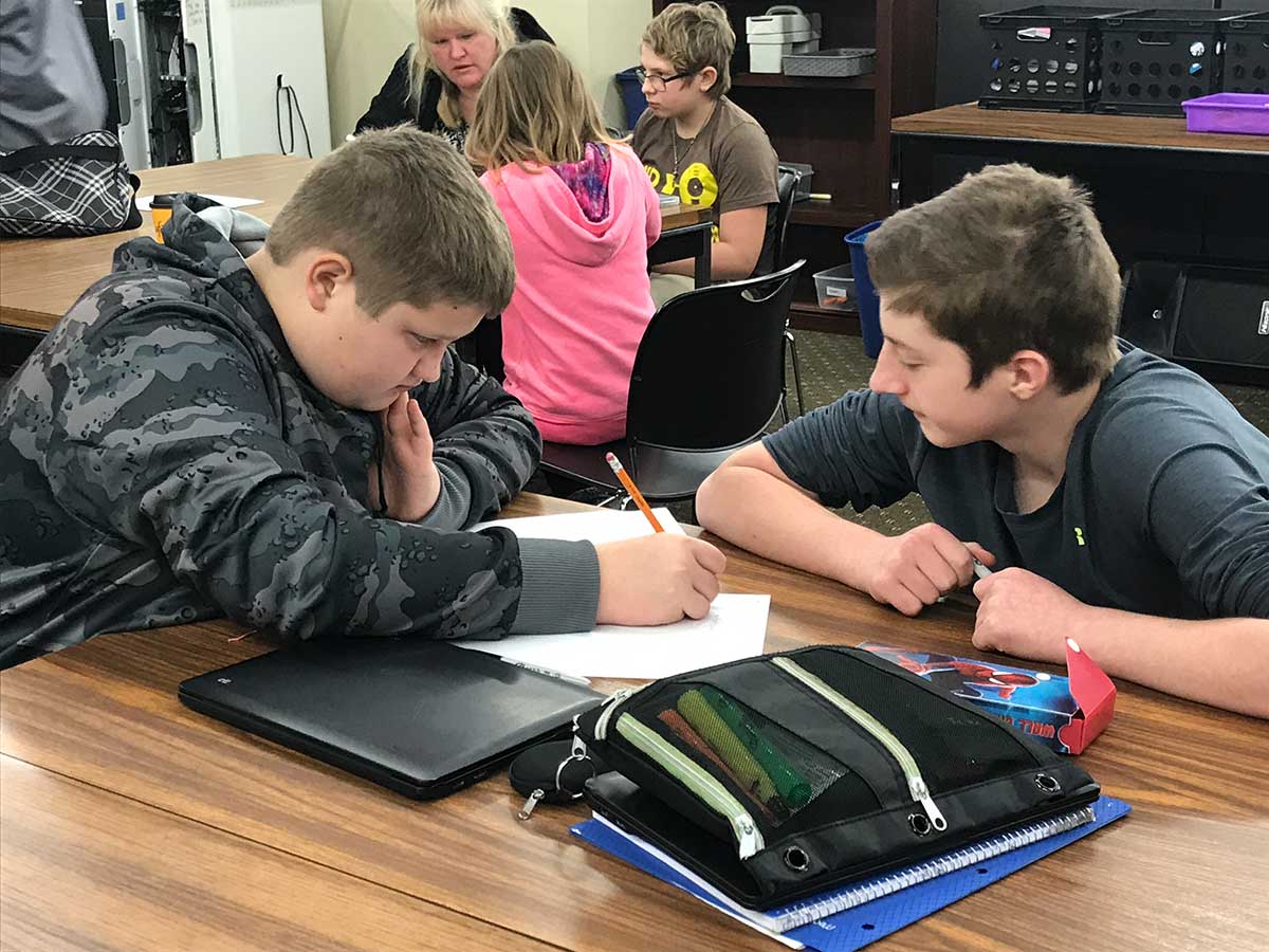 Two boys writing at a classroom table.