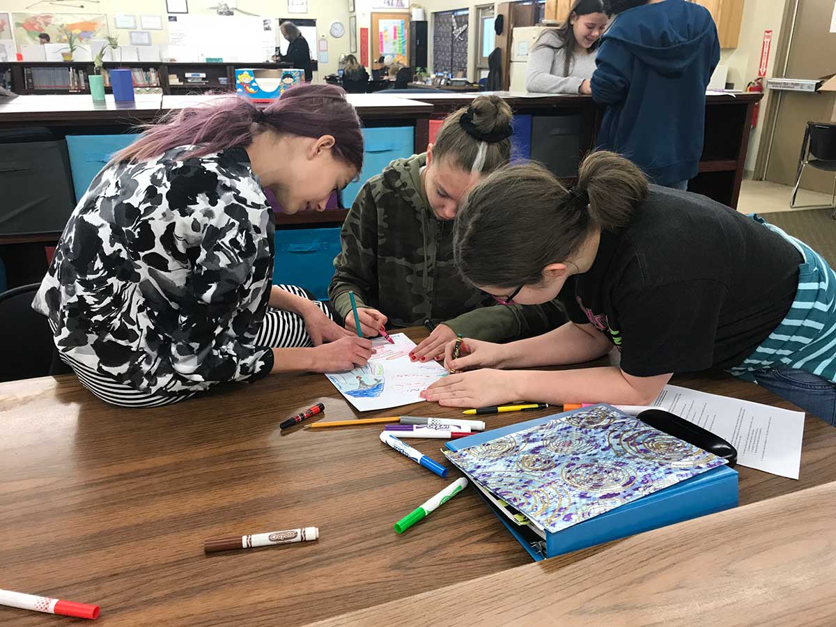 Three girls collaborating on a project at a table.