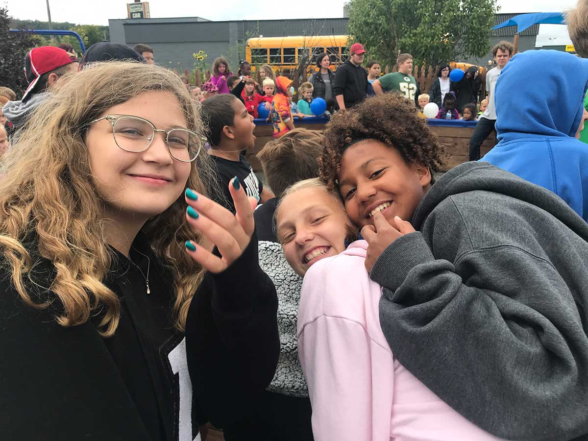 Three girls smiling and hugging at a school event.