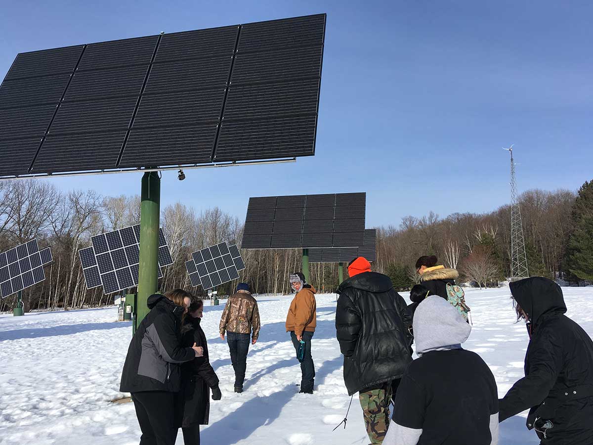 Group of people standing in snow near solar panels, enjoying winter scenery.