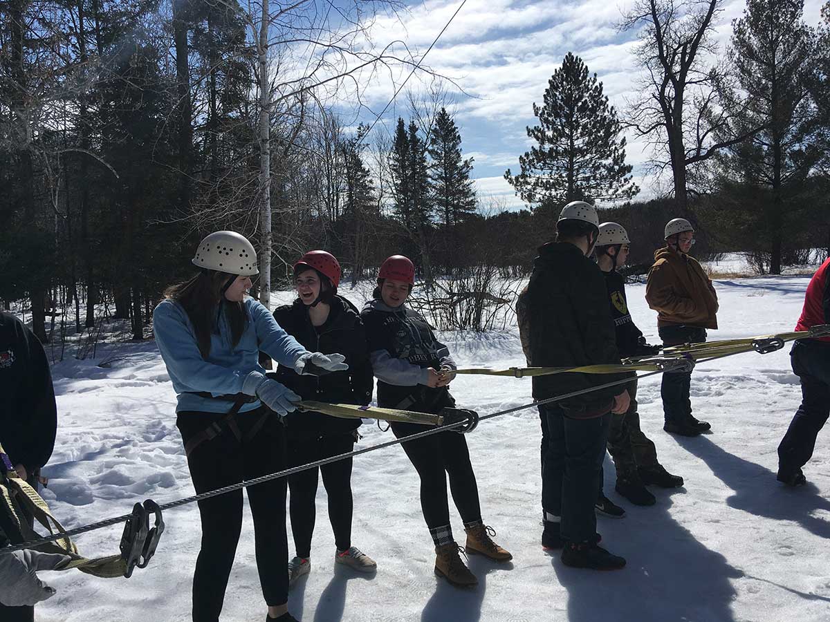 A diverse group of people standing around a rope, ready for a team-building activity.