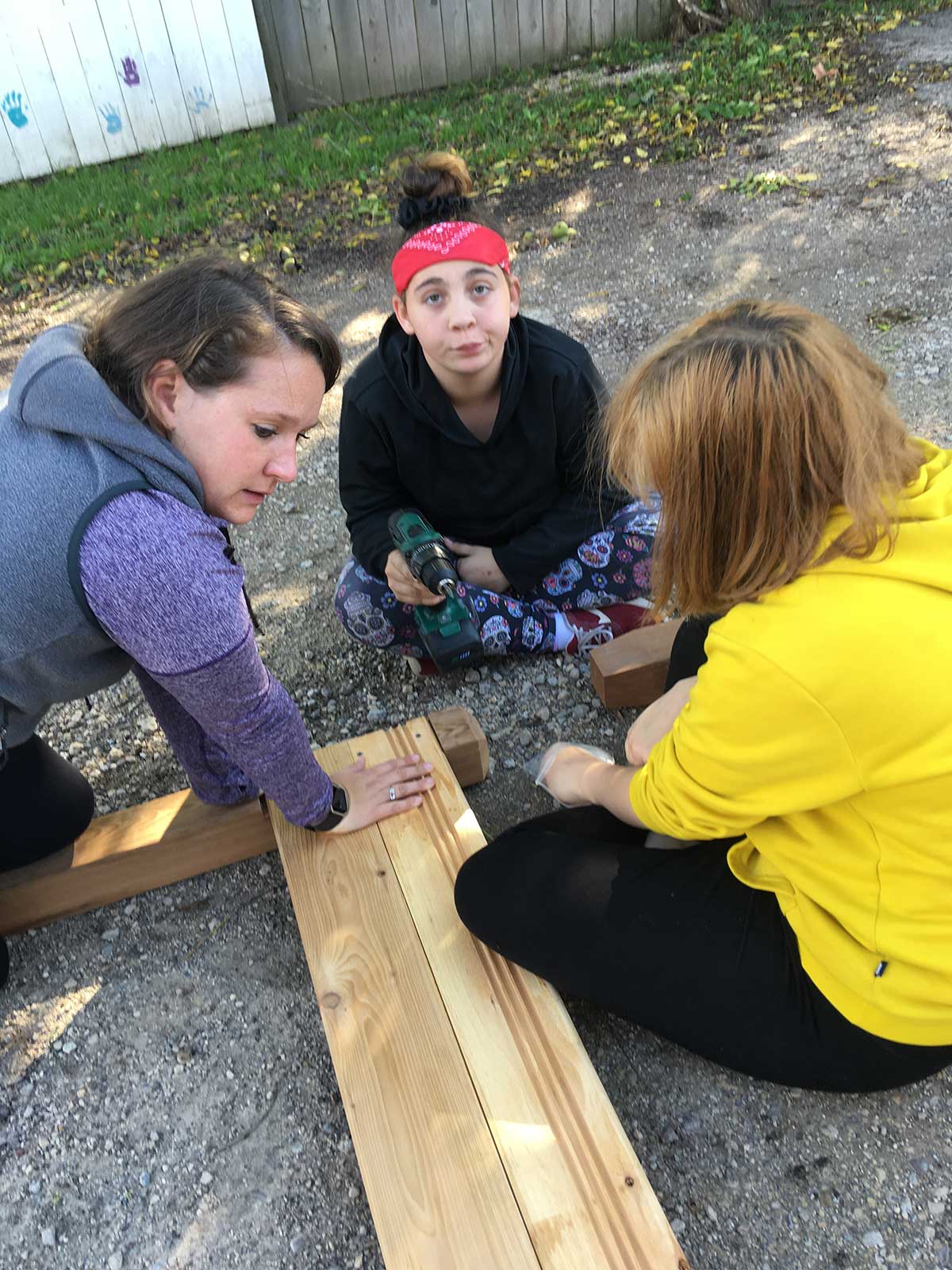 Three women working on a wooden bench.