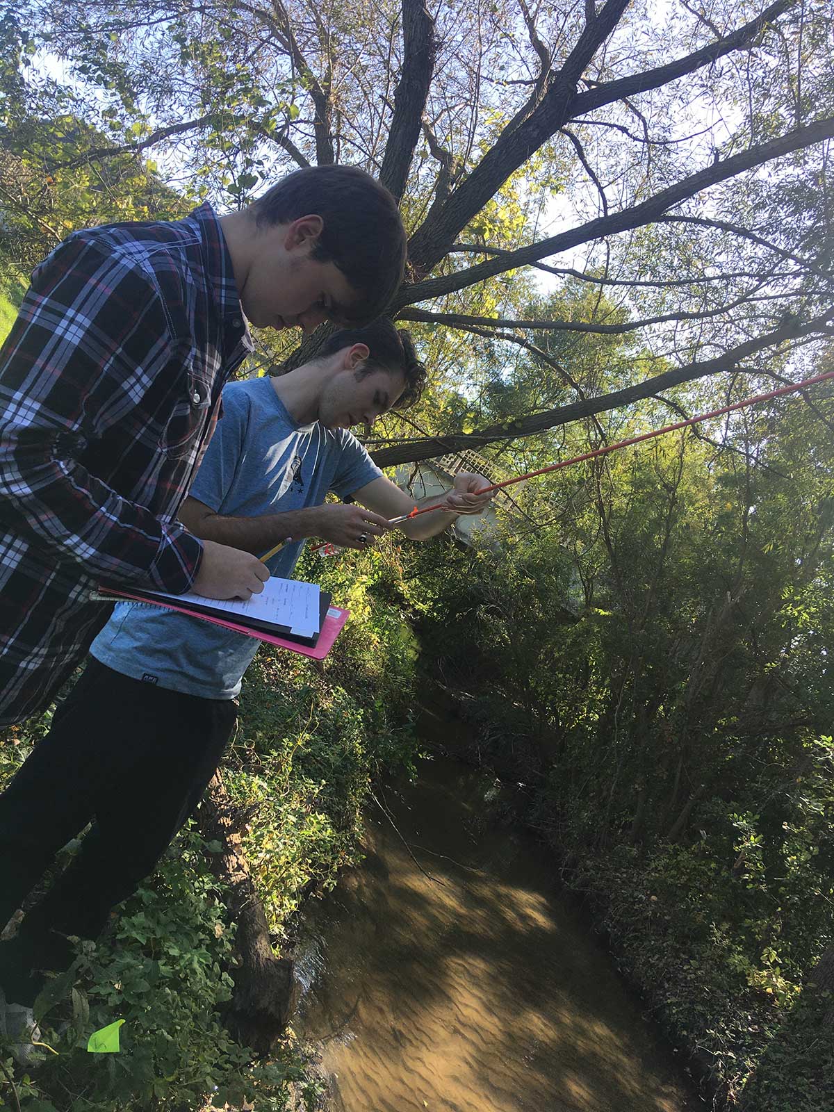 Two young men standing by a stream, enjoying the peaceful nature around them.