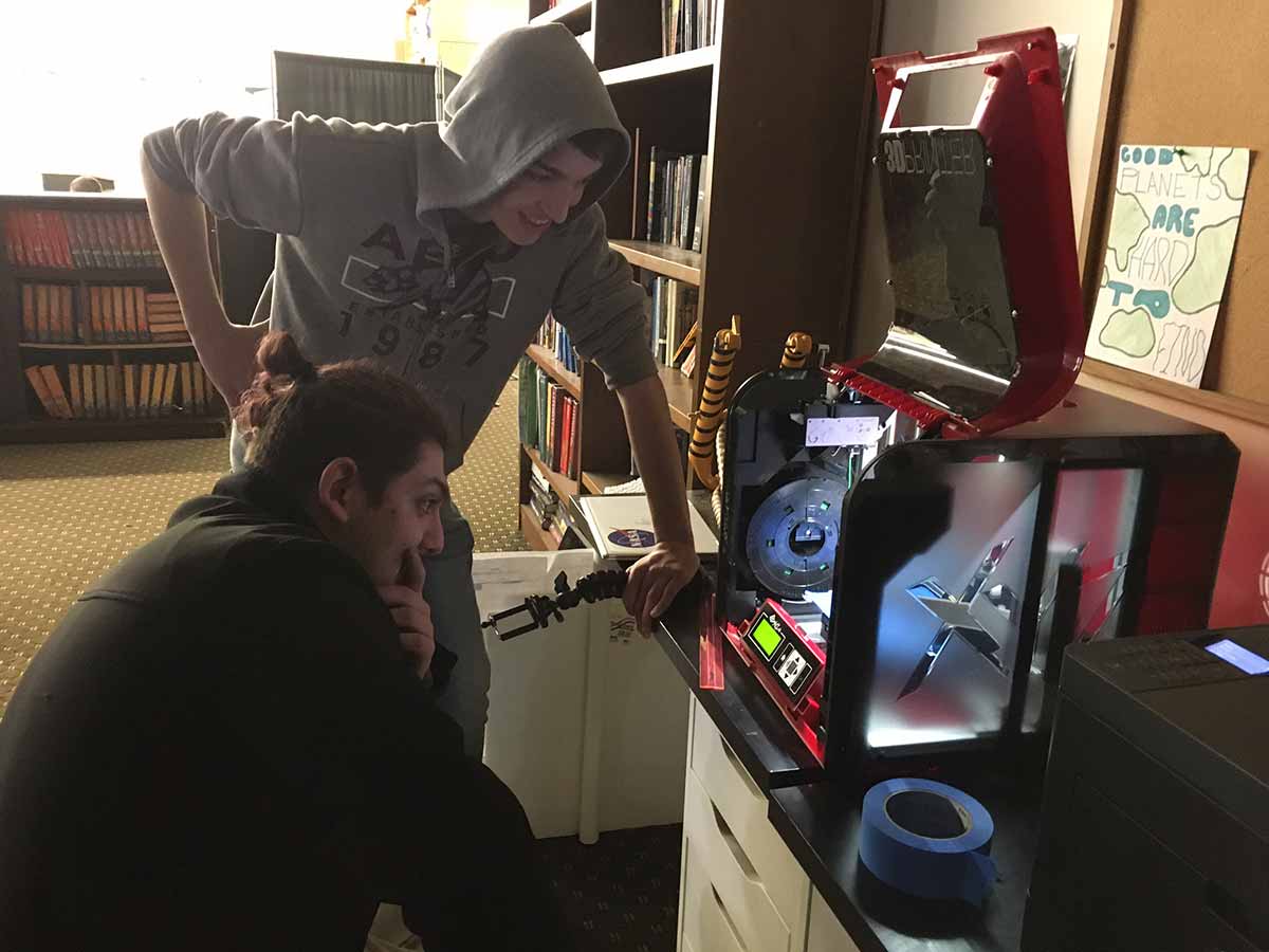 Two men examining a 3D printer in a library.