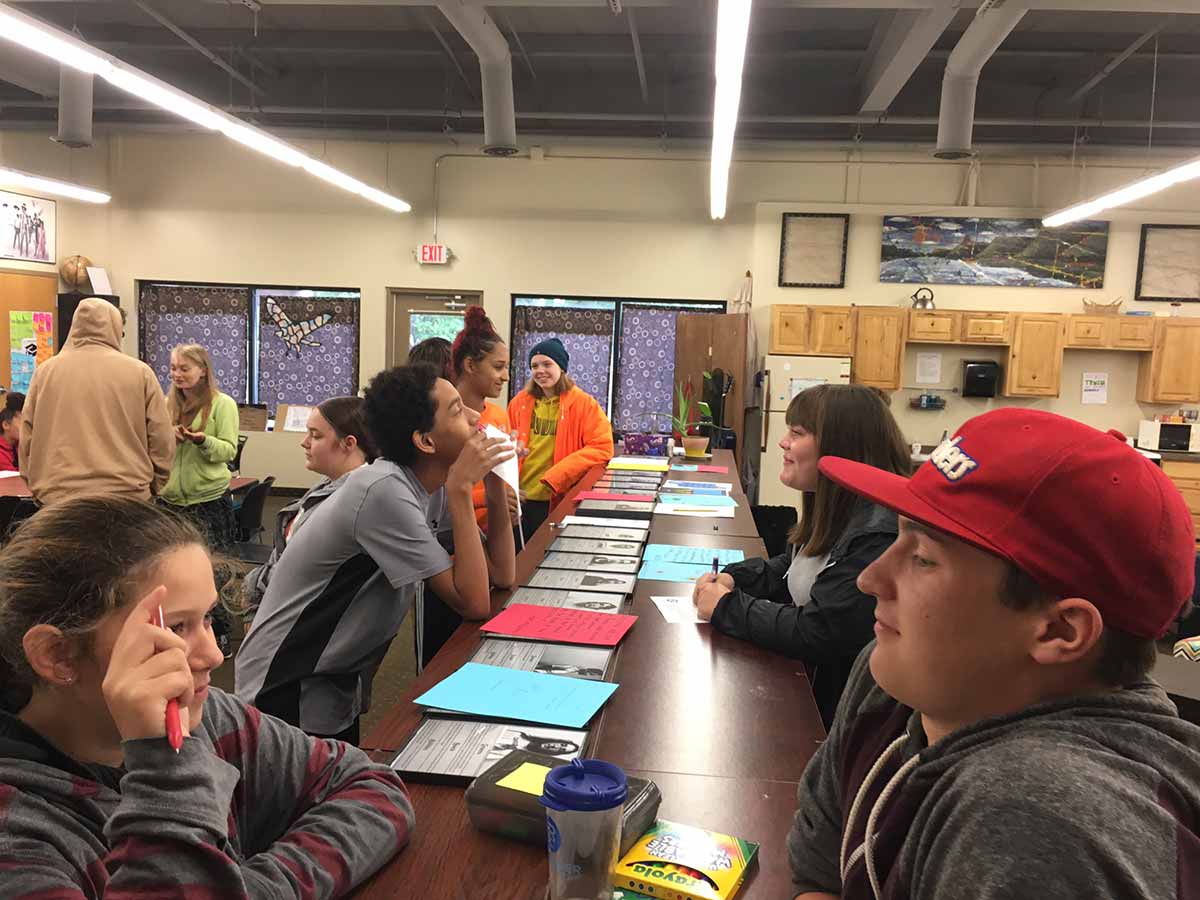 Group of students sitting at table with notebooks, studying together.