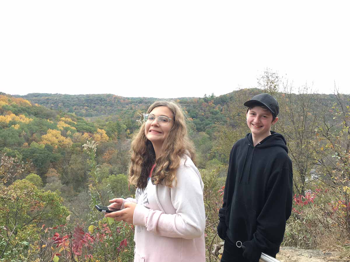 Two people standing on hill, looking at woods.