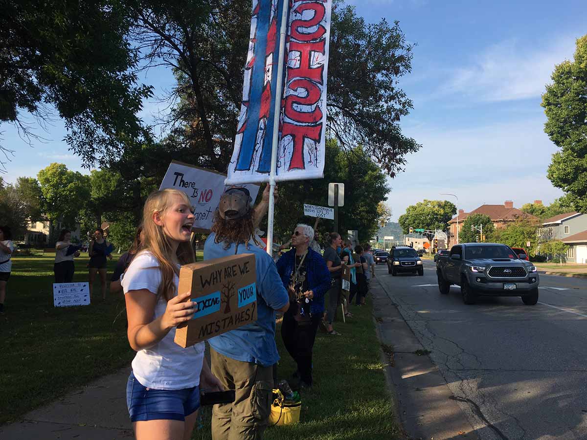 A woman holding a sign in front of a diverse crowd at a protest.