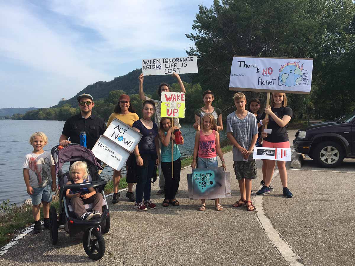 A diverse group of people holding signs by the water, advocating for environmental protection.