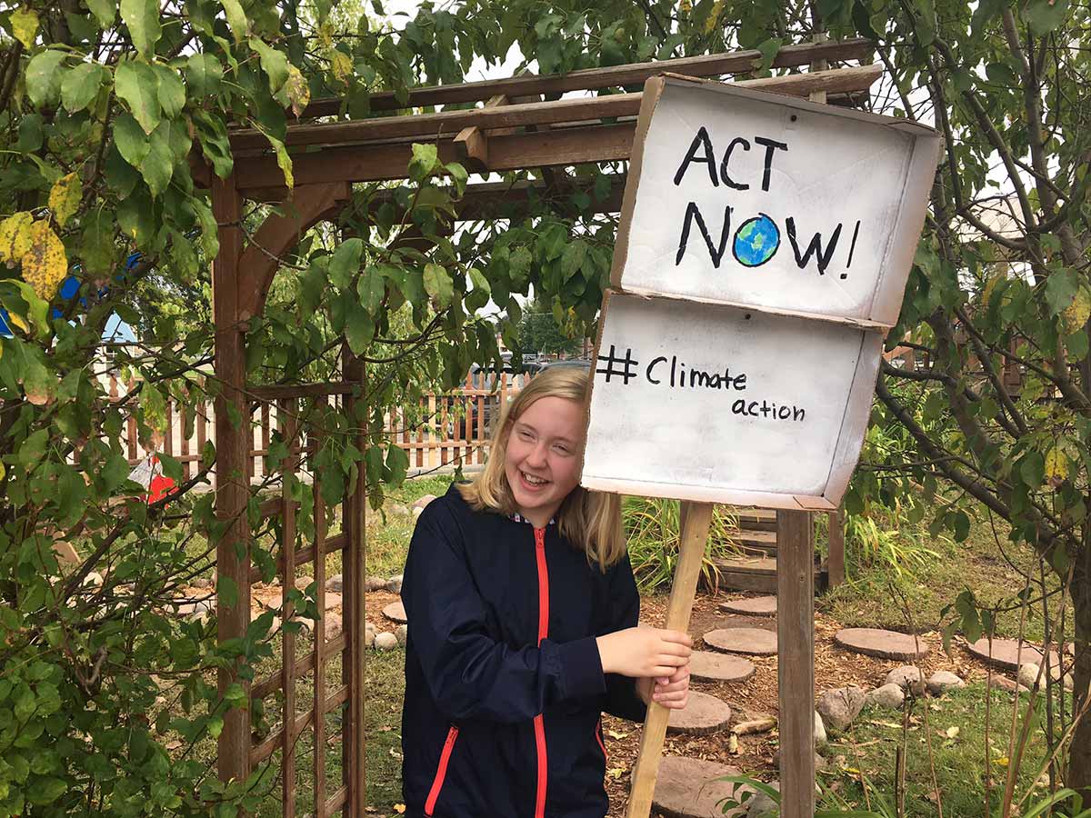 Young girl holding a sign that says "Act Now" with determination.