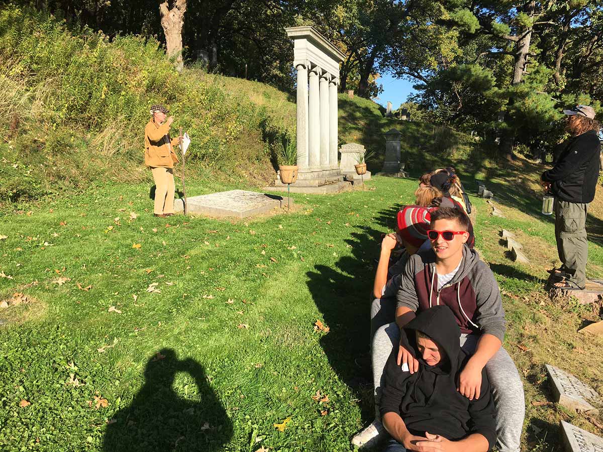 A somber group sitting on grass near a grave, paying respects.