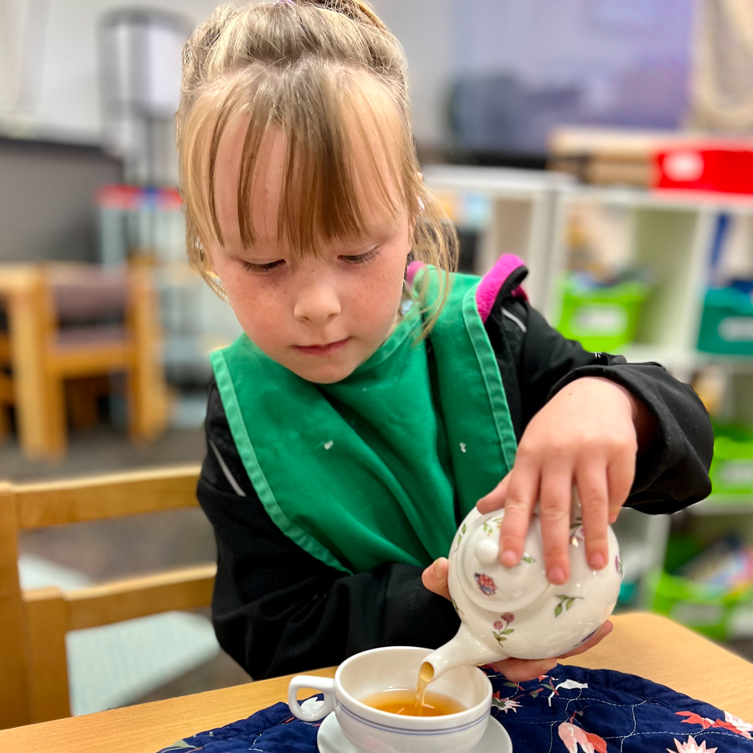 Young girl pouring tea in her classroom.