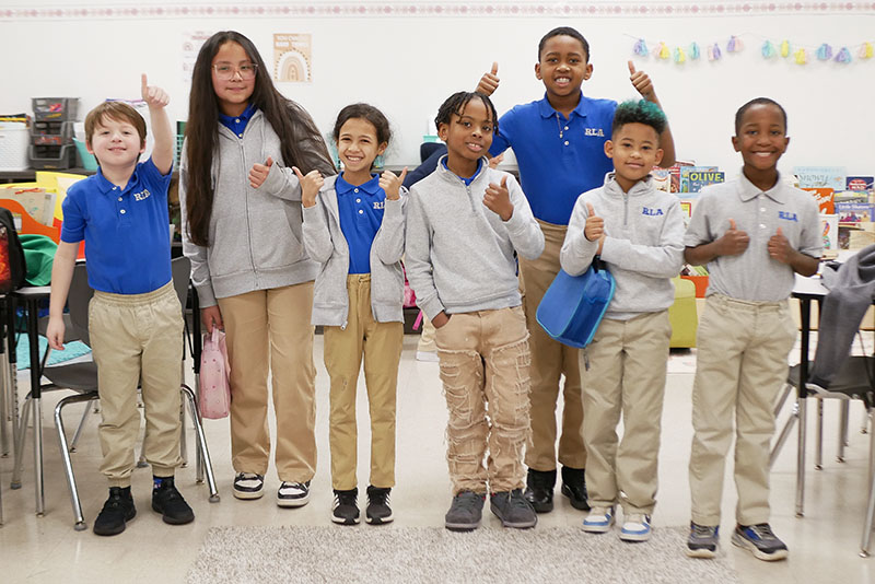 A group of elementary school students give a thumbs up.