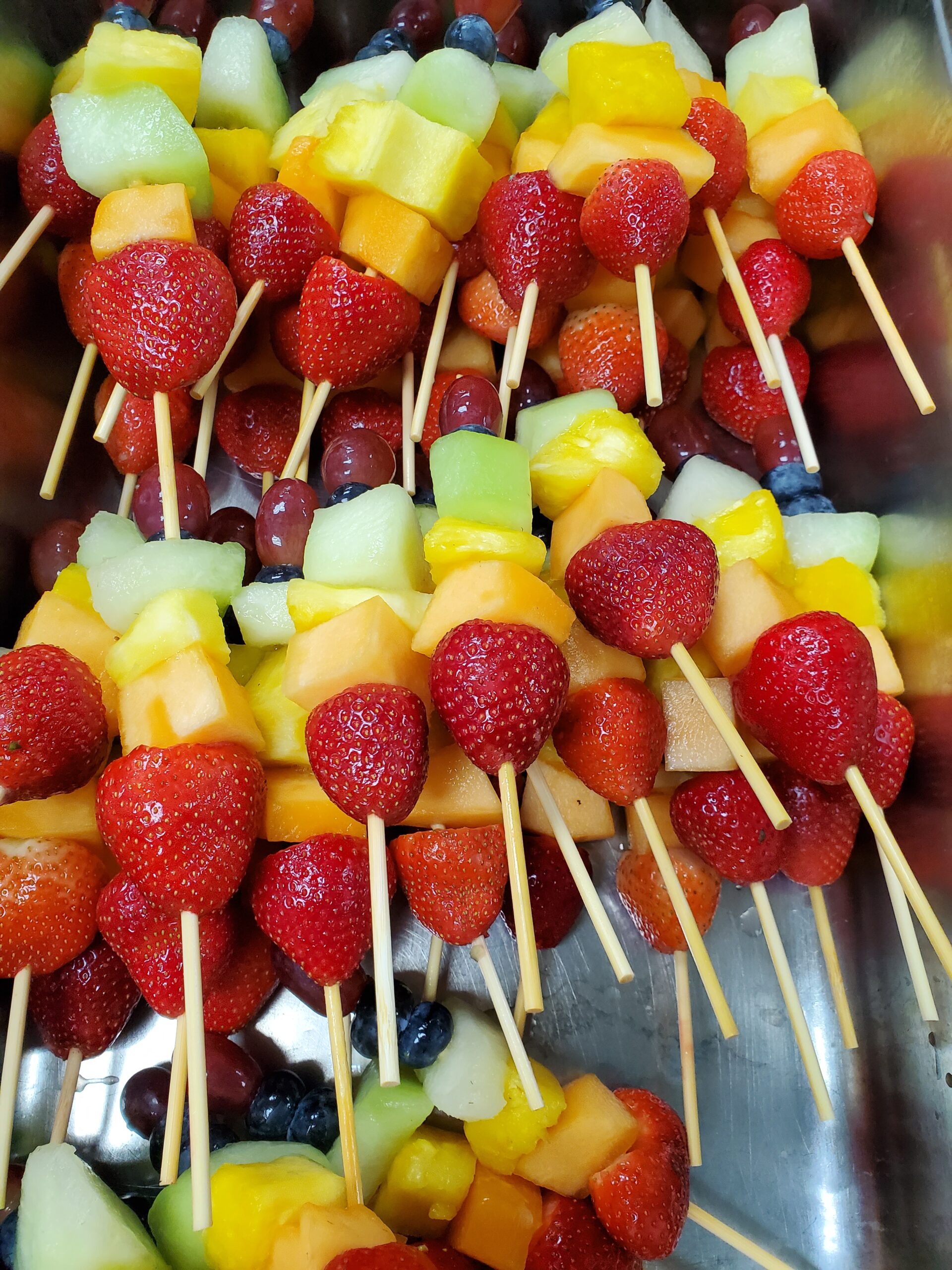 Fruit skewers are arranged on a silver platter